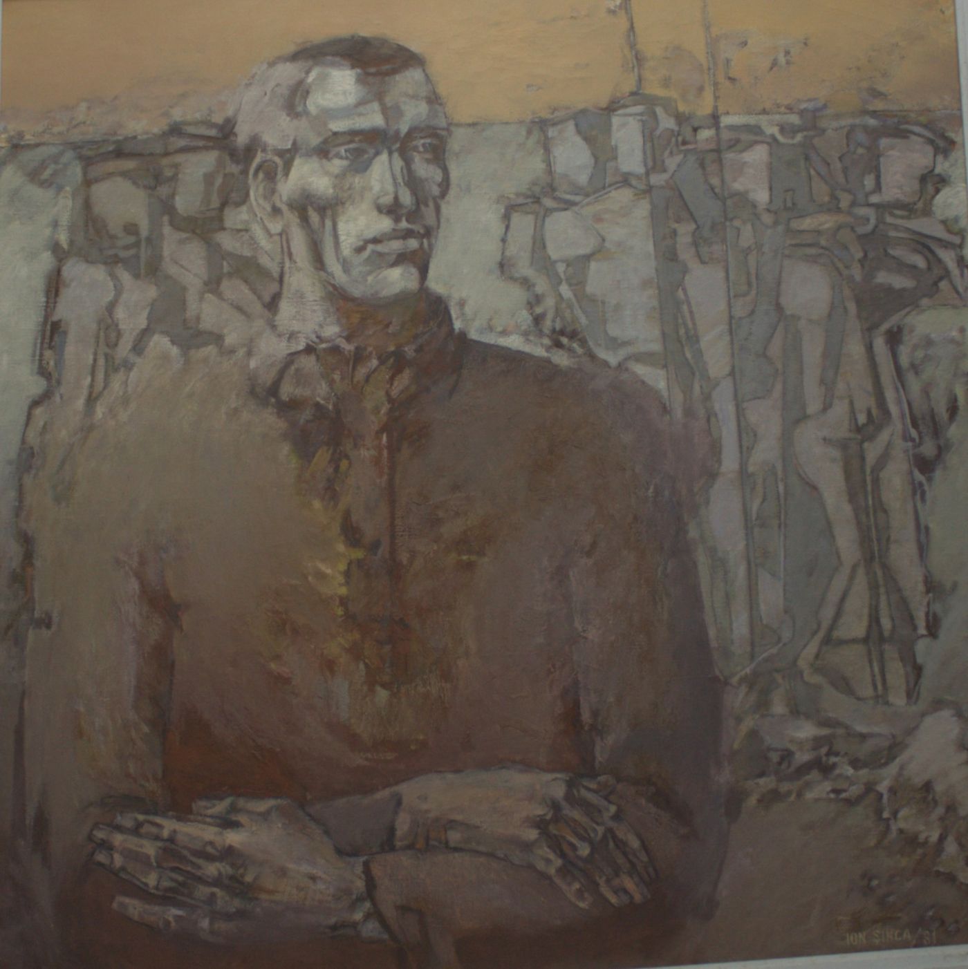 Portret frontal al unui bărbat masiv, cu brațele încrucișate, pe un fond de siluete cenușii de muncitori.